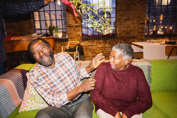 Playful senior couple reacting to mistletoe on Christmas Front view of casually dressed man and woman in early 60s sitting on sofa in loft apartment with sprig overhead and humorous facial expressions. inside of flash stock pictures, royalty-free photos & images