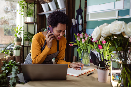 Mid adult woman taking an order from a custom on a phone call. She is working in a flower shop.