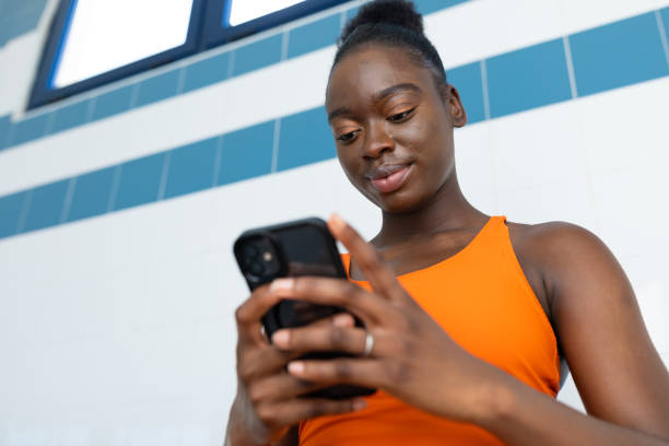 istock Black young woman using her smartphone, sitting in a bench at the swimming pool 1614373777