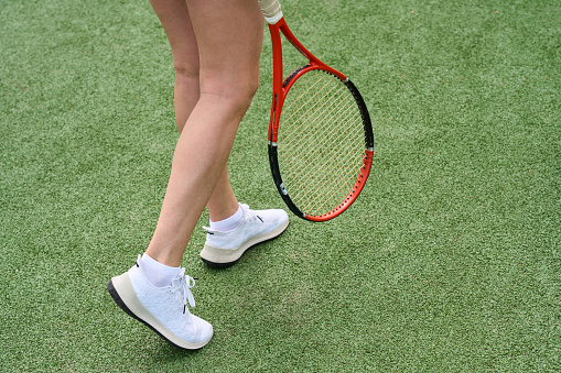 Woman with beautiful legs walks along the tennis court, she has a tennis racket in her hands