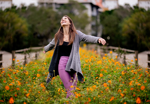 Carefree young woman laughing and dancing alone in a field of colorful flowers outside in a public park