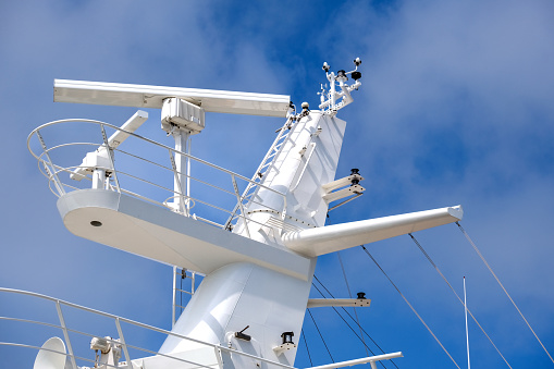Radar antennas, sensors, and other technical structures above the bridge of a large and modern ship against a blue sky