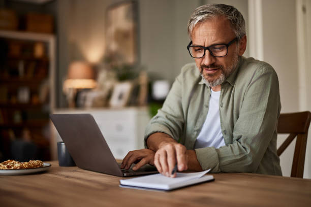 istock A mature male freelancer checks the notes in a notebook while working on a laptop. 1614430313