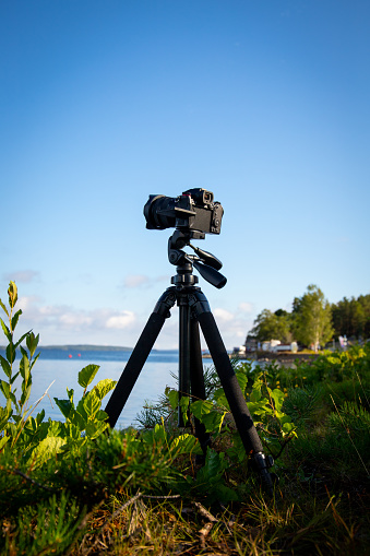 camera mounted on tripod at beautiful lake scenery during day. blue sky and clouds on background.