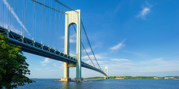 High resolution stitched panoramic image of the Verrazano-Narrows Bridge on a spring morning. The bridge connects boroughs of Brooklyn and Staten Island in New York City. It was built in 1964 and is the largest suspension bridge in the USA. Historic Fort Wadsworth is next the bridge foot. Canon EOS 6D full frame censor camera. Canon EF 50mm f/1.8 II Prime Lens. 2:1 Image Aspect Ratio. The image was stitched from 2 rows of images. This image was downsized to 50MP. Original image resolution is 82MP or 12,793 x 6,396 px.