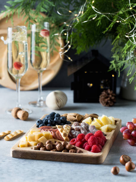 istock Wooden plate with various snacks on the New Year's table. Assorted cheeses, sausages, nuts in a menazhnitsa. 1614441896