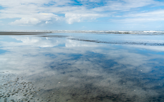 Billowing clouds are reflected in the shoreline sand in Moclips, Washington.