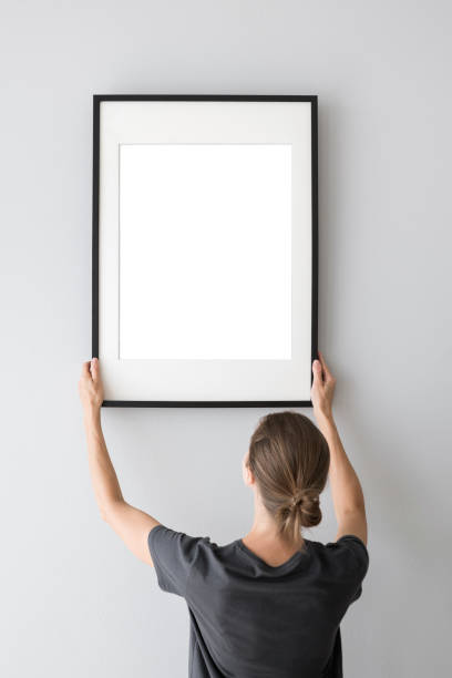 istock Woman holding blank picture frame against a wall. Artwork mock-up concept 1614457785
