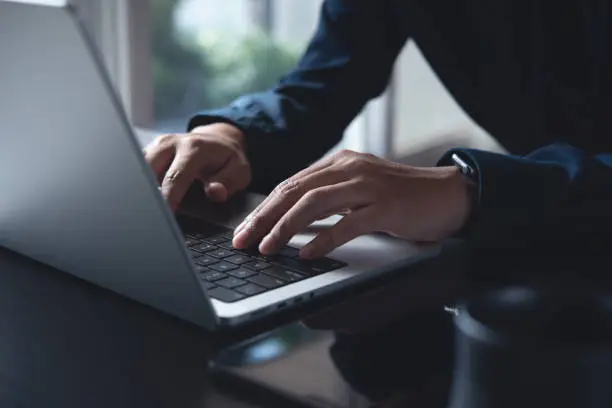 Business man hands typing on laptop computer keyboard, searching information, surfing the internet on dark office desk, distance job, online working, business and technology concept