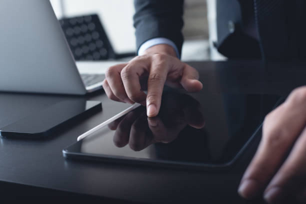 istock Businessman in black suit using digital tablet and  working on laptop computer on table at office. Business man finger touching on tablet screen at desk and suring the internet, close up 1614461071