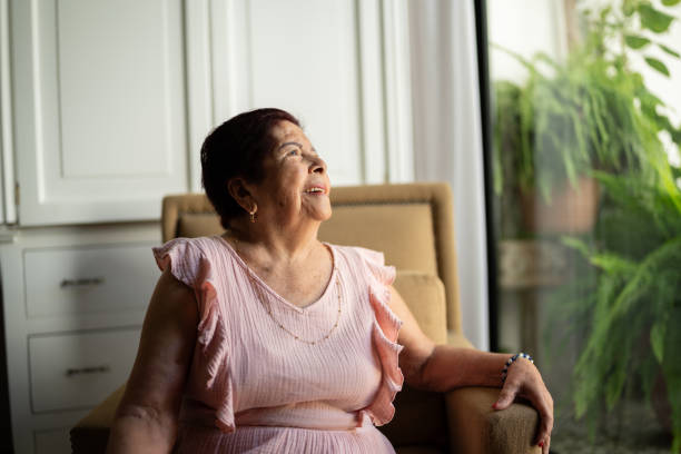 istock Senior woman looking through window contemplating at home 1614465486