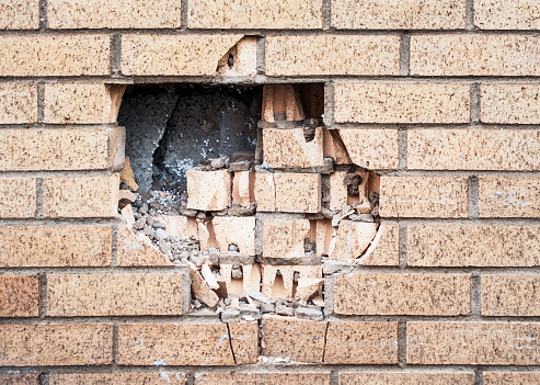 A large hole in a brick wall, with cracked and damaged bricks remaining