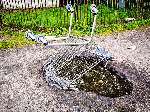 A supermarket trolley left upside down over a puddle on a run-down city path.