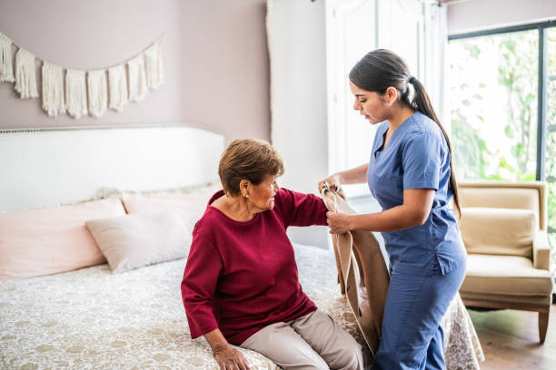 home caregiver assisting a senior woman to get clothed in a nursing home - ouderenzorg stockfoto's en -beelden