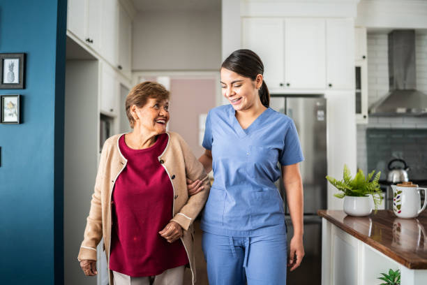 home caregiver helping senior woman to walk at house - ouderenzorg stockfoto's en -beelden