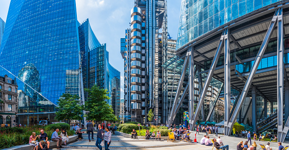 Office workers and tourists relaxing at lunchtime in a square between the futuristic skyscrapers of the City of London Financial District.