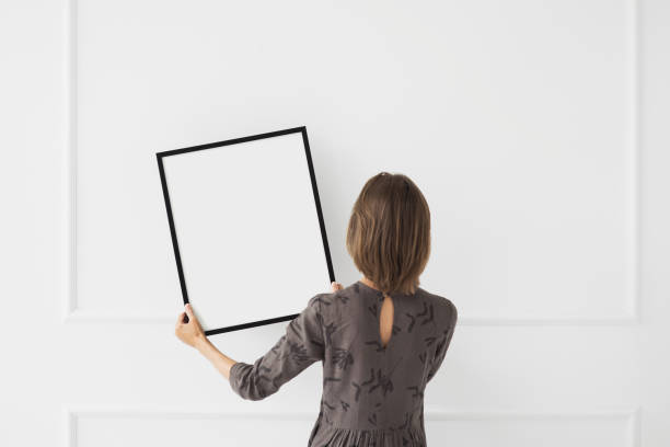 istock Woman holding blank picture frame against a wall. Artwork mock-up concept 1614527742
