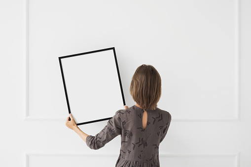 Young woman hanging an artwork, blank empty frame mockup