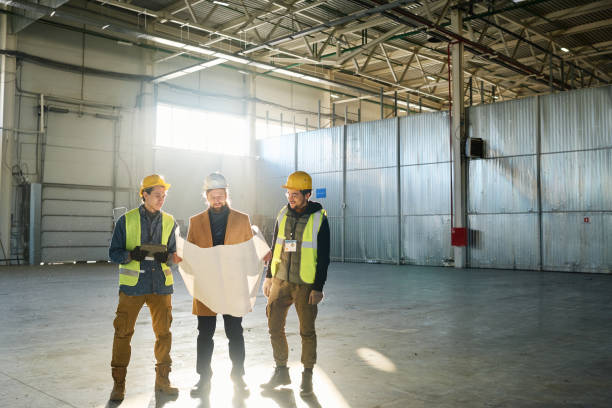 istock Three engineers in protective helmets discussing blueprint with building plan 1614564047