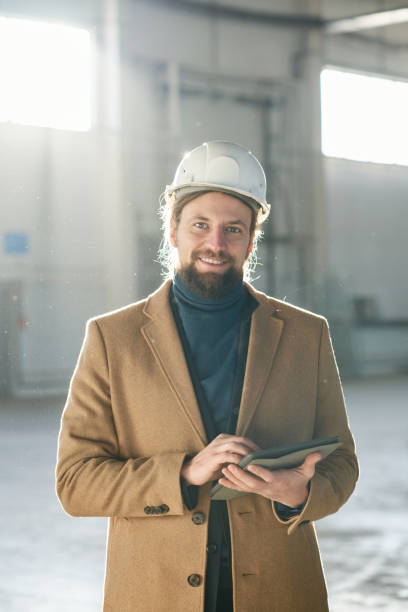 istock Young successful contractor or foreman in safety helmet and beige coat 1614564604