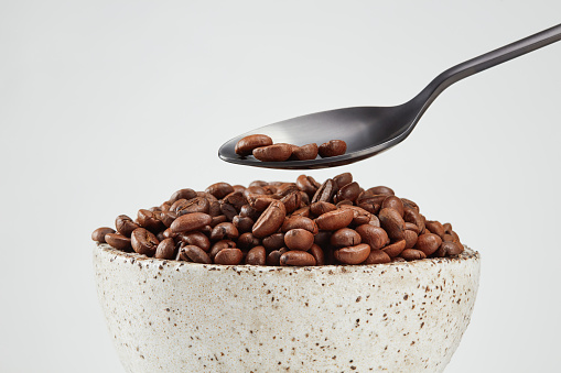 Put coffee beans from a spoon into a pile in a bowl on a white background. Selective focus