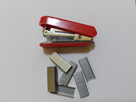 A small red stapler  and staples on a white background  as office equipment  for used to staple a small amount of paper.