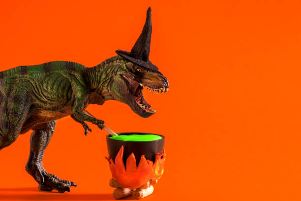 istock Dinosaur wearing witch hat is brewing potion in pot on orange background. Halloween greeting card. 1614651544