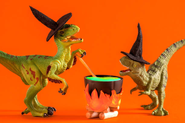 istock Two funny dinosaurs wearing witch hats are brewing potion in pot on  orange background. Halloween greeting card. 1614652052