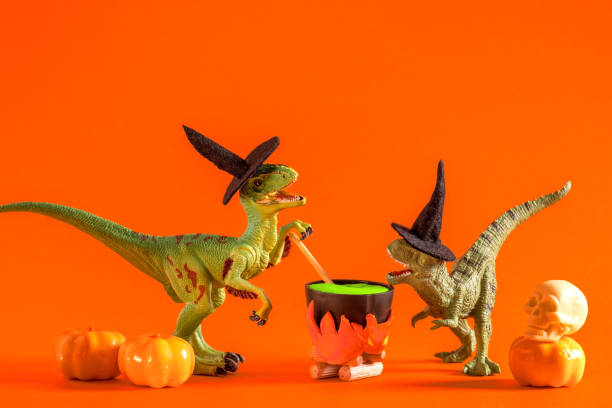 istock Two funny dinosaurs wearing witch hats are brewing potion in pot on  orange background. Halloween greeting card. 1614652068