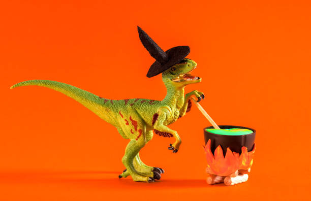 istock Dinosaur wearing witch hat is brewing potion in pot on orange background. Halloween greeting card. 1614652076