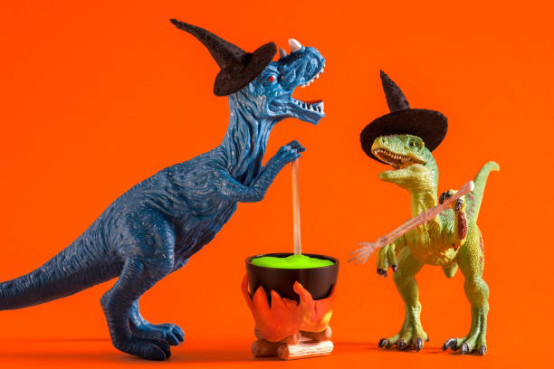 istock Two funny dinosaurs wearing witch hats are brewing potion in pot on  orange background. Halloween greeting card. 1614652091