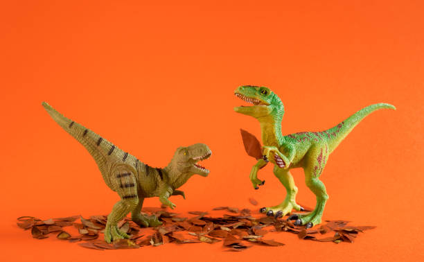 istock Two green dinosaurs playing with autumn leaves. 1614653682