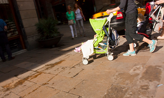Young woman pushing baby stroller on a crosswalk. Barcelona, Catalonia, Spain. Copy space available.