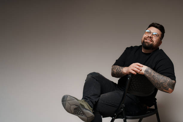 istock Bearded and tattooed man sitting on chair in studio 1614699883