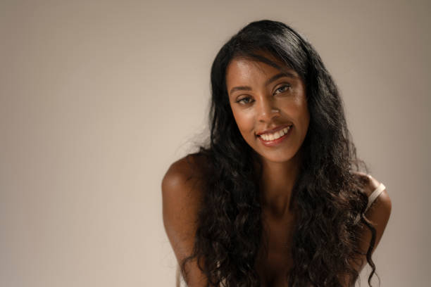 Tall slender African American model with long hair and casual dress poses in studio before a white seamless background.