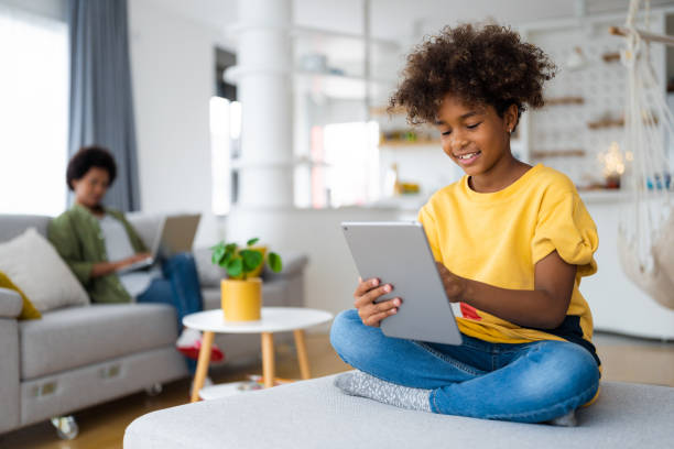 Carefree smiling African American young girl with curly hair using digital tablet