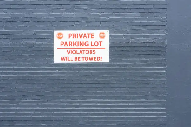 Brick wall, painted dark gray containing sign with text, STOP.  PRIVATE.  STOP.  PARKING LOT.  VIOLATORS WILL BE TOWED!  Red and white sigh on wall.