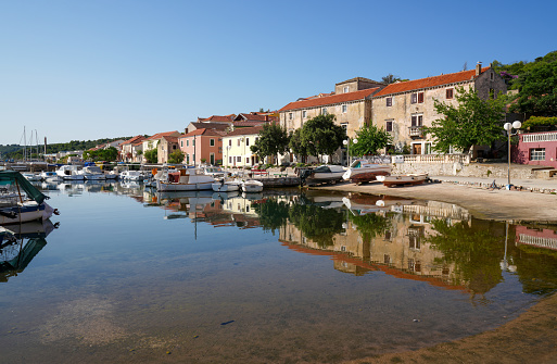 The small town Saly reflection in his port water. It is  on Long Island (Dolgi otok), what is in central Dalmatia coast not far from big Town Zadar on Croatian mainland. A lot of boats in water, houses and trees reflection in water with blue sky in background. Adriatic Sea as part of Mediterranean.