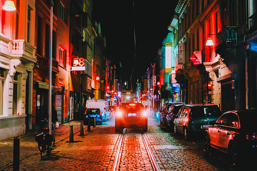 a car driving in a night european city with night lights and neons on cobblestones, shot from behind