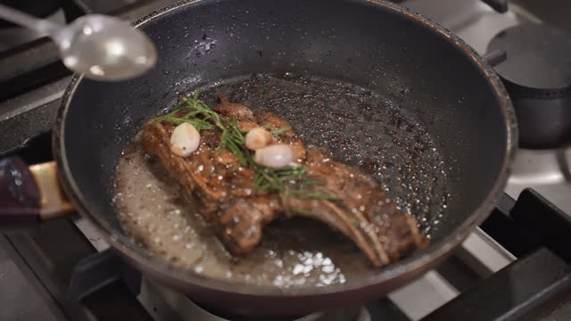 Close up wagyu beef striploin steak with pepper on dark pan in kitchen. Searing beef brisket steak on the electric stove with seasoning with garlic, pepper. Fry the meat in a frying pan. Chef preparing and spicing meat restaurant kitchen.