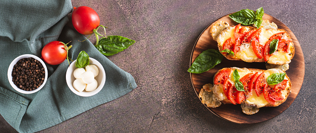 Baked brioche sandwiches with tomatoes, mozzarella and basil on a board top view web banner