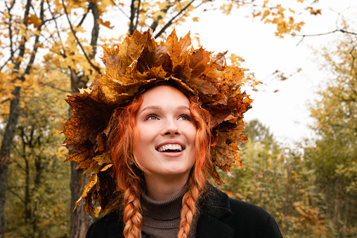 Brunette woman in a wreath of maple leaves in a dress on the background of an autumn park or forest.