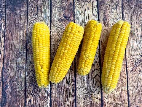 Freshly cooked delicious sweet corn on a wooden brown table. Boiled cobs of sweet corn on a wooden table. Appetizing healthy natural food. Top view of yellow corn