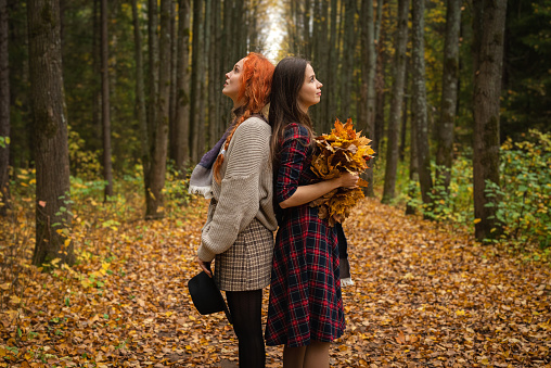 Two happy female friends are walking through the autumn forest in beautiful clothes.