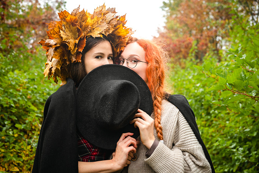 Two happy female friends are walking through the autumn forest in beautiful clothes.