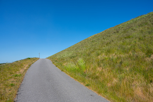 Narrow asphalt road up a steep grass hill.