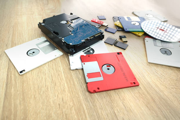 istock vintage retro electronic data storage devices from the 80s, 90s, cd disk, flash drives, modern hard disk scattered on table. Stack of floppy disks in grey, black, blue, yellow, red, white 1614850794