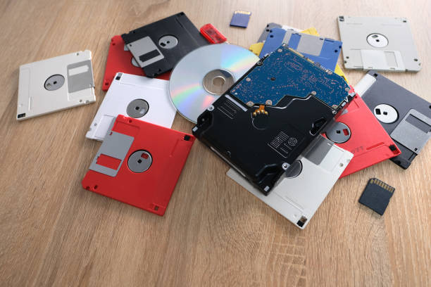 istock vintage retro electronic data storage devices from the 80s, 90s, cd disk, flash drives, modern hard disk scattered on table. Stack of floppy disks in grey, black, blue, yellow, red, white 1614850795