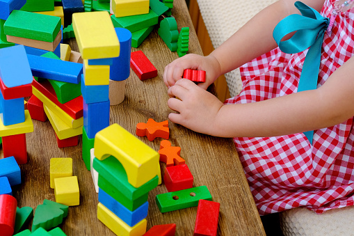 little four year old boy has fun playing at home with wooden blocks building tower under isolation, development of fine motor skills, simulation is the leading activity of children