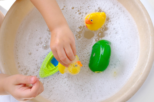 happy child, toddler 3 years old plays with rubber yellow duck for swimming, children's hand close-up, toy in soapy foam, concept of bathing, playing with water, baby hygiene, healthy lifestyle